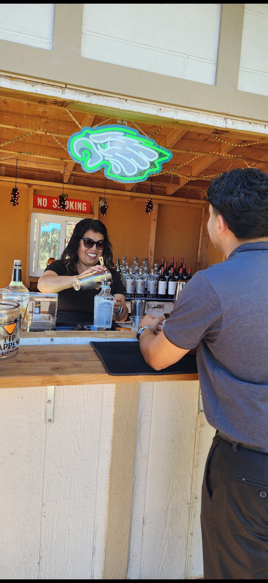 Sip Happens bartender in sunglasses pouring a drink from a shaker for a guest at the mobile bar